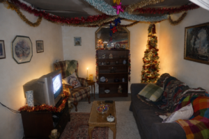 Installation view of a domestic interior featuring vintage 1980s furniture, Christmas decorations, soft lighting and sound-based elements.