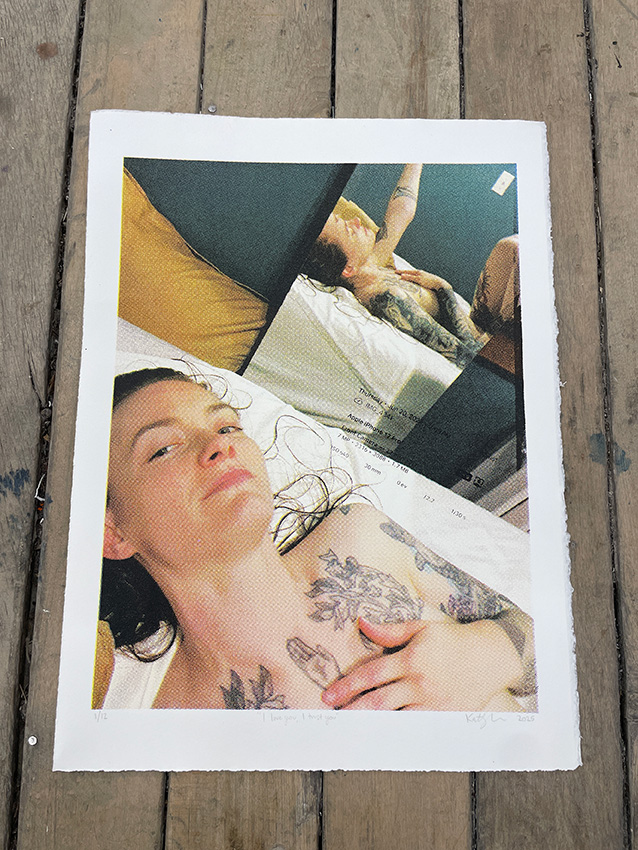 photo of a CMYK screen print photographed on a wooden floor. The image that was screen printed is a selfie taken on a phone. The woman is on a bed, nude but covered up by her hand and angles. Her reflection is in the background.