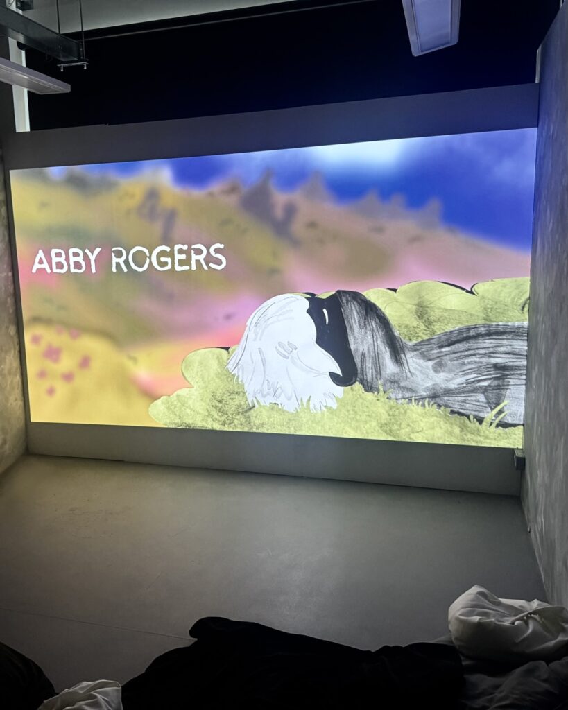Projection of the credits to the film. The main character is laying in grass and the words ‘ABBY ROGERS’ are in bold white text.