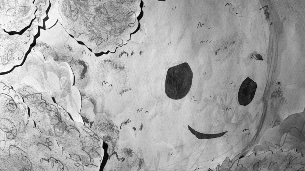 Black and white film still featuring a close up of a smiling giant who is surrounded by and made up of grass, trees, and bushes.