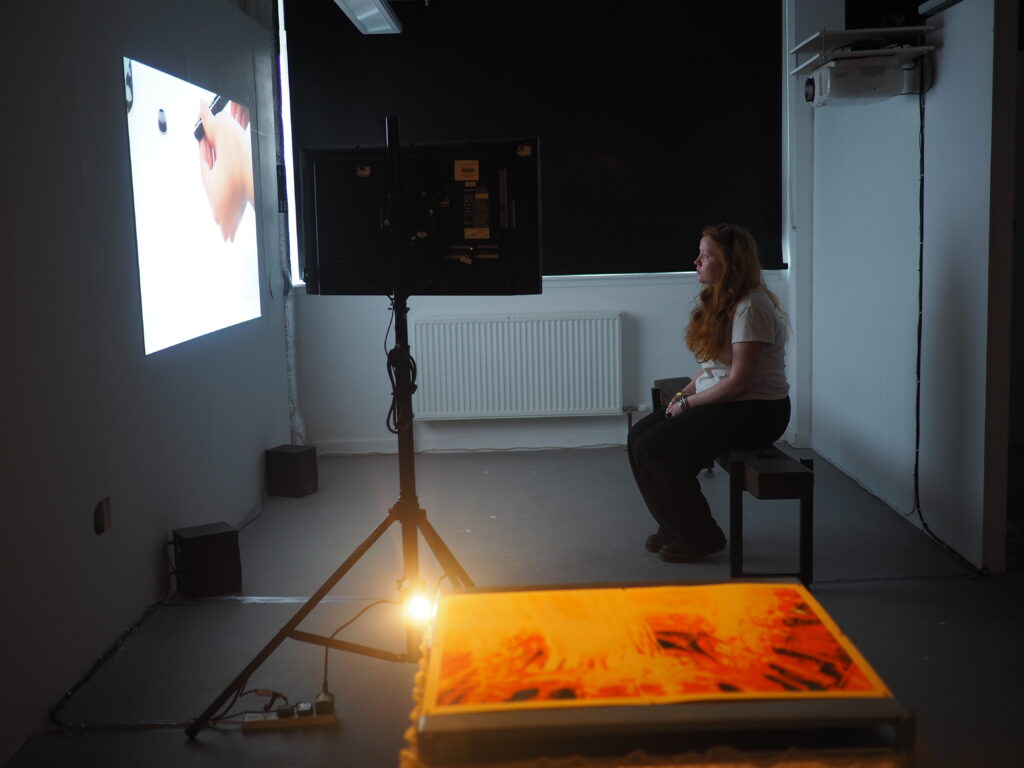 Woman sat on a bench watching a projector and a monitor screen