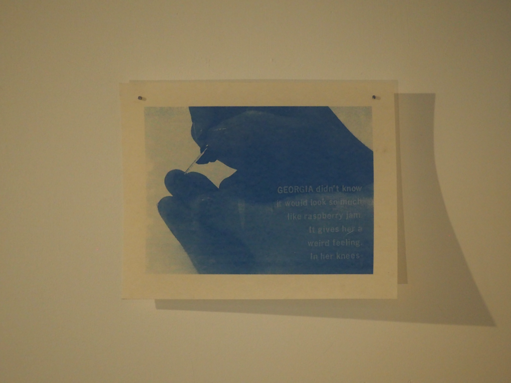 translucent print of a blue hand tattooing itself hung from the wall by nails