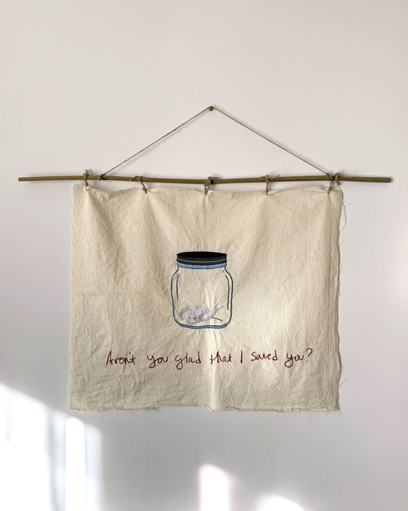 Hand stitched tapestry with bird inside glass jar and text that reads "Aren't you glad that I saved you?"