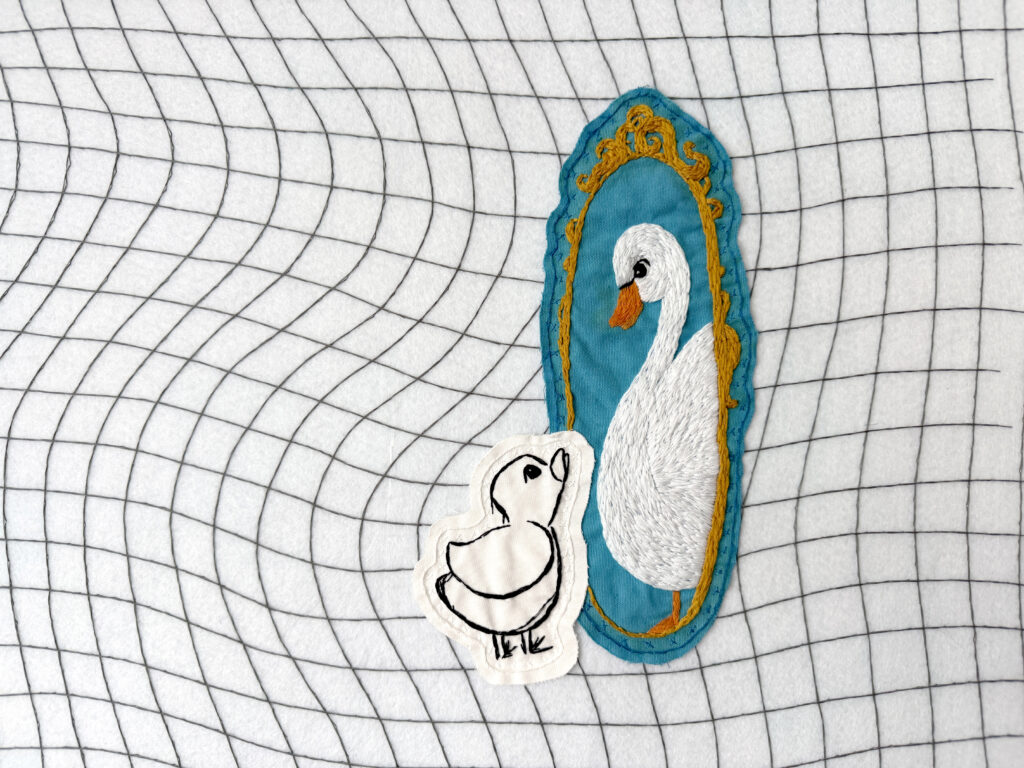 Hand embroidery with small duck looking into a mirror and seeing a swan
