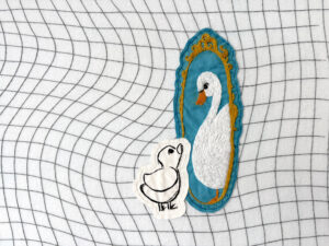 Hand embroidery with small duck looking into a mirror and seeing a swan