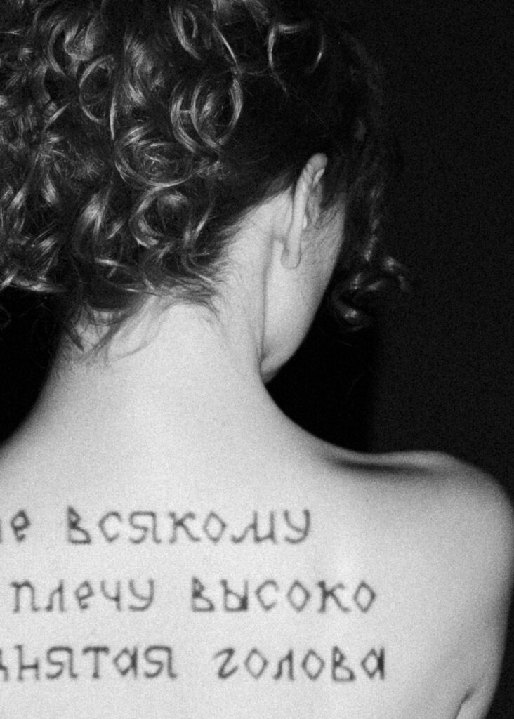 Black and white photograph of a person seen from behind, with handwritten Cyrillic text across their upper back.