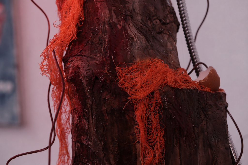 Close-up detail of a red illuminated pillar-like sculpture with layered silicone textures, exposed wire, and glowing internal light.