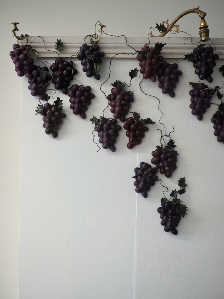 A wax grapevine growing off wire vines attached to brass fixtures on a white skirting ridge.